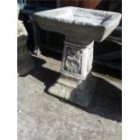 A concrete square topped birdbath.