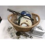 A wicker basket containing various items cutlery, cheese dish and plates.