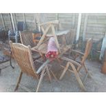 A teak folding garden table and five chairs with a parasol.