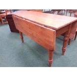 A Victorian pine drop-leaf table resting on turned supports.