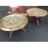 A pair of Indian benares brass tiffin tables resting on wooden supports smaller of the two