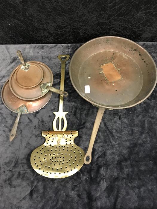 A brass chestnut roaster, three copper saucepan lids and a large copper saucepan.