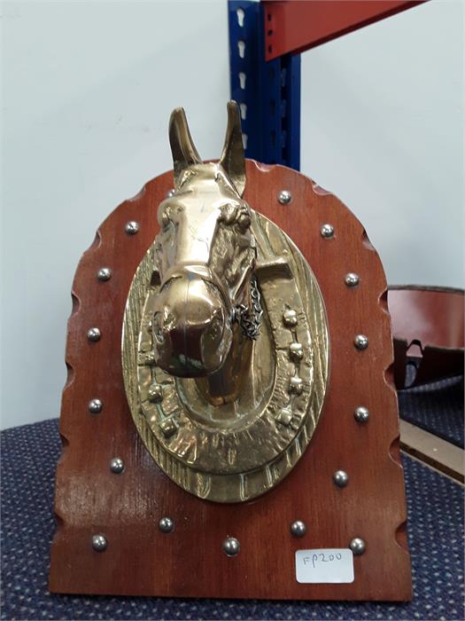 A wooden plaque depicting a brass horse's head.