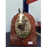 A wooden plaque depicting a brass horse's head.