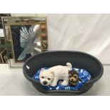 A dog basket together with a picture of a dove and two ornamental dogs.