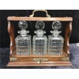 A three bottle Tantalus in oak frame with brass mounts. (Examine).