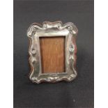 A small antique silver roll and scroll decorated photo frame on wood back. (5.5 inches by 4.5