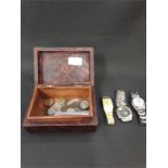 A wooden box containing coins and three wristwatches.