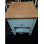 A modern white bedside table with drawer and shelf underneath.