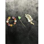 A circular arts and crafts brooch set with multicoloured stones and one other. leaf form set blue