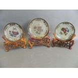 A garniture of three Chinese plique-à-jour saucer dishes with floral decoration, on carved wood