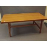 A 1970s teak topped refectory style dining table, raised on square supports united by a stretcher,