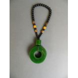 A Chinese spinach jade pi-disc pendant on a black bead string, pendant 2½"