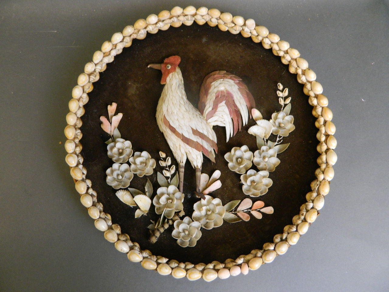 A basket work and shell plaque depicting a cockerel amongst flowers, 14" diameter