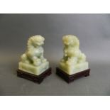 A pair of celadon green hardstone ornaments carved in the form of kylin, on a pair of matched carved