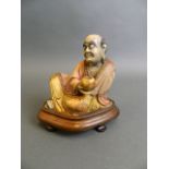 A Chinese carved soapstone ornament in the form of a seated immortal, mounted on a hardwood stand,