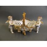 A Dresden porcelain centrepiece in the form of two cherubs with a pierced basket, 13" long