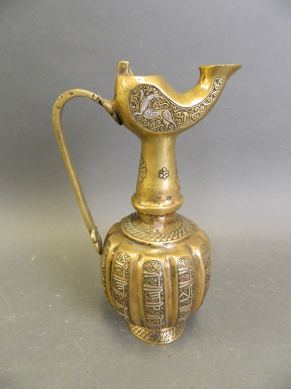 An Islamic polished bronze pourer with silver inlaid decoration, 8½" high (lacks lid)