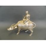 A Chinese mixed metal ornament of a traveller riding a buffalo, 11" long