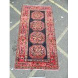 A Persian Hamadan Luri carpet with bespoke medallion design on a red and ebony field, 52" x 102"