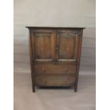 A 1930s oak gentleman's press cupboard with two cupboards fitted with slides over drawers, raised on