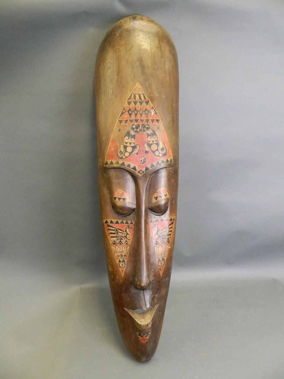 A large African carved wood wall mask with painted animal decoration, c1950, 9½" x 40"