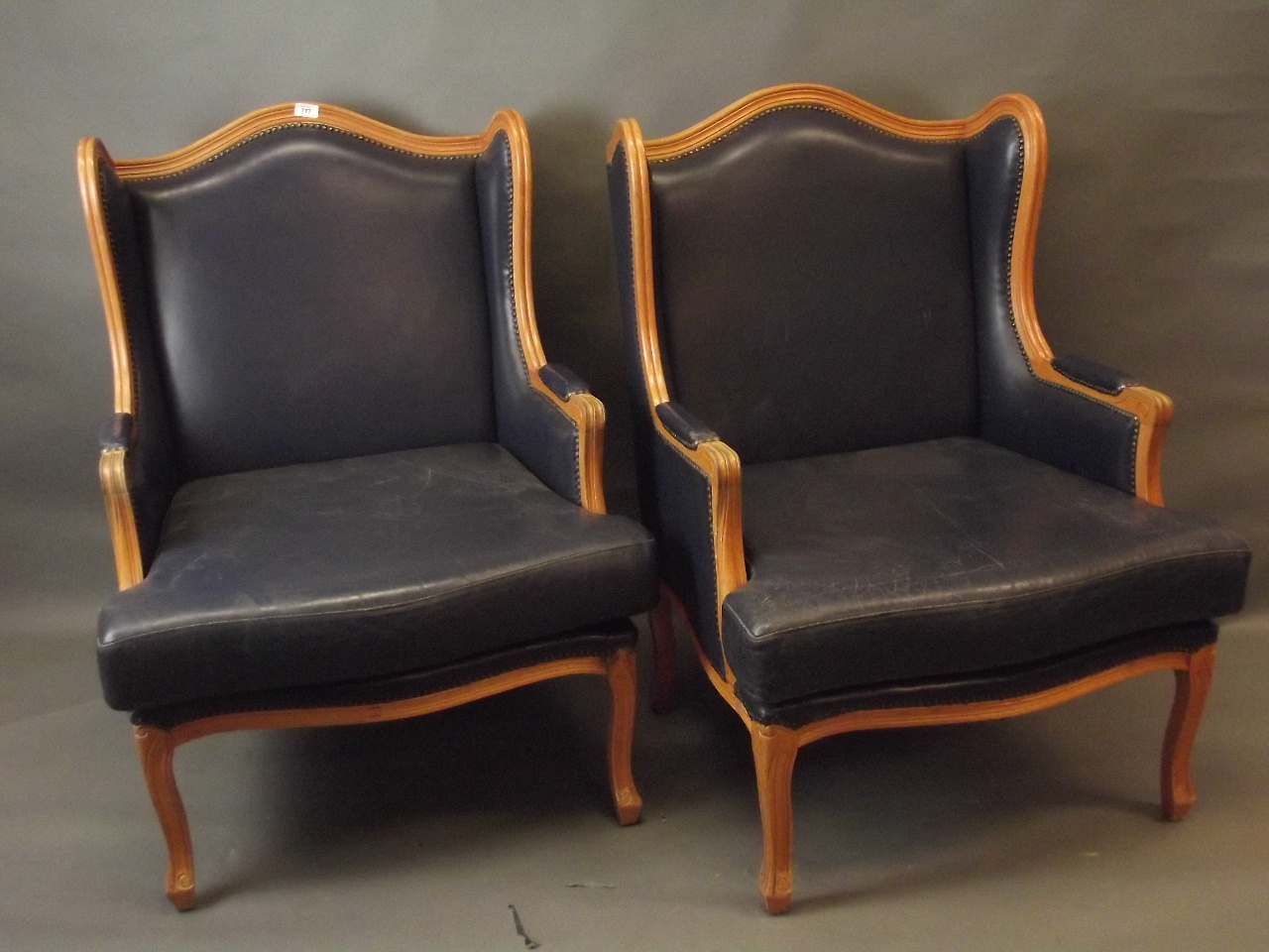 A pair of French style beech wood framed winged armchairs with leather cushions and upholstery