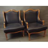 A pair of French style beech wood framed winged armchairs with leather cushions and upholstery