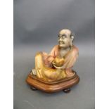 A Chinese soapstone figure of a reclining immortal, mounted on a hardwood stand, 5½" high