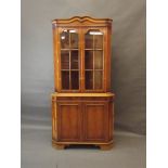 A yew wood corner display cabinet with glazed upper section over cupboards, raised on bracket