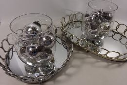 Two cast metal oval and circular mirrored trays and a collection of glass baubles