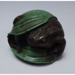 Figure of a frog with stone set eye sheltering beneath a leaf,