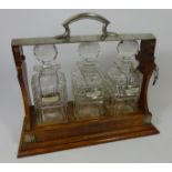 Edwardian three bottle Tantalus with cut glass decanters. Retailed by Rowe Jewellery, Marlow.