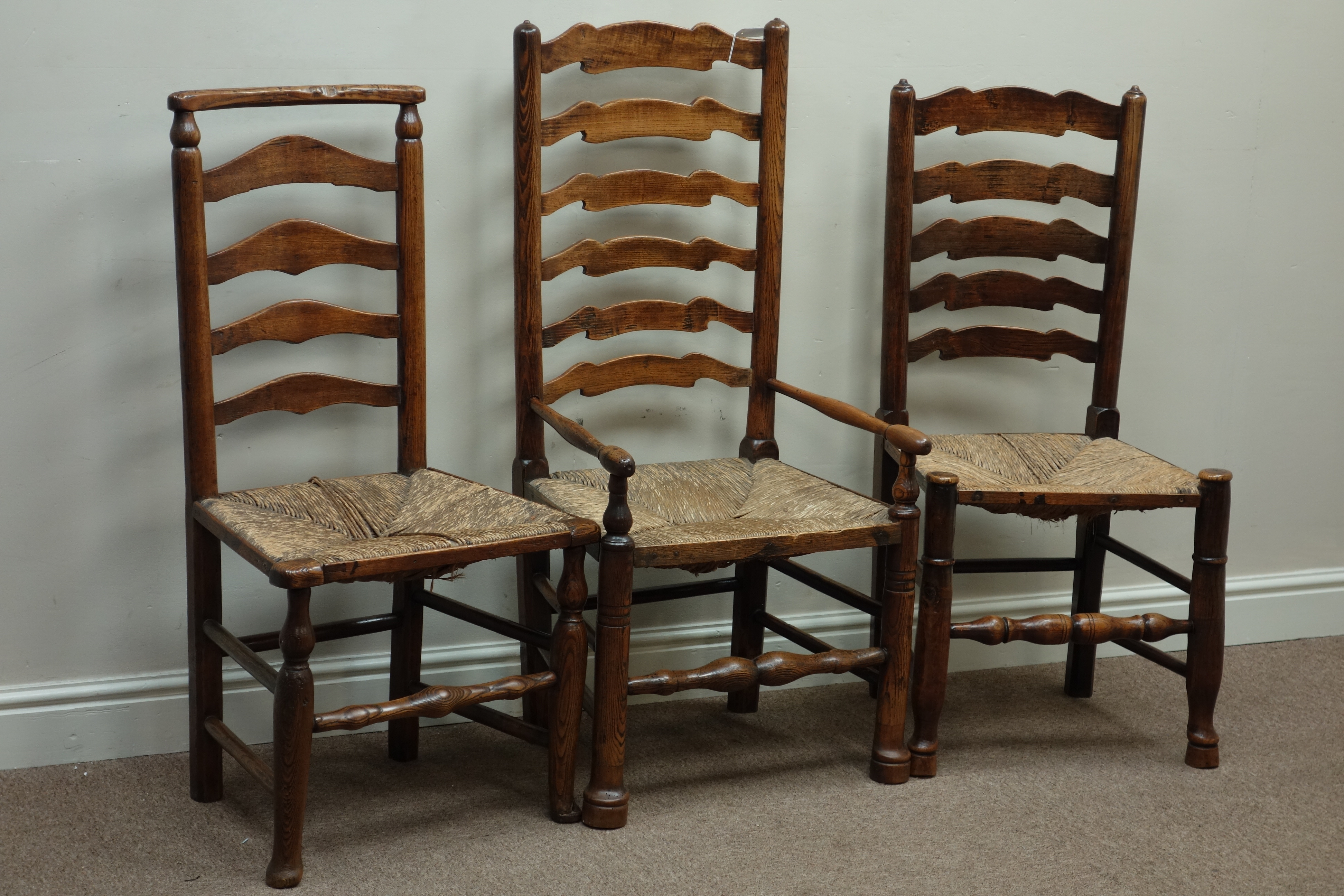 Three early 19th century country elm and oak ladder back chairs with rush seats Condition