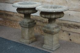 Pair of hand carved stone gadroon urns with leaf rim carvings, on plinths, D61cm,