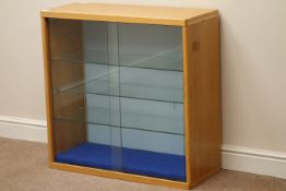 Light oak illuminated display cabinet enclosed by two sliding glass doors, adjustable glass shelves,