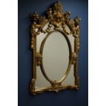Ornate gilt framed wall mirror decorated with floral baskets and cherubs, oval centre,