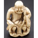 A Japanese ivory netsuke of a Rakan seated upon a holding his robes at his shoulder and knee,