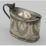 An oval silver mustard pot engraved with floral swags, blue glass liner,