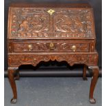 A carved oak slope front bureau on stand with cabriole legs.