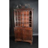 A George III mahogany cabinet with broken swan neck scrolling pediment, over two lancet glaze doors,
