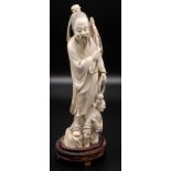 A Chinese ivory carving of a standing Lohan holding a bamboo cane and a rosary,