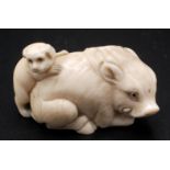 A Japanese ivory netsuke, a recumbent boar with a dog trying to climb upon its back, signed.