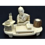 A Japanese ivory okomono, an artist holding a paint brush and seated behind a low table,