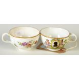 A pair of German porcelain cups, each enamelled with a cherub holding a silhouette cartouche,