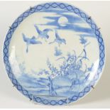 A Japanese blue and white Arita charger decorated with three swans flying over a river scene with