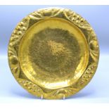 A brass Arts and Crafts dish with a fruit decorated repousse rim and planished centre, impressed F.