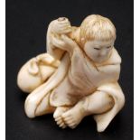 A Japanese ivory okimono, a youth seated and holding his hands at shoulder height,