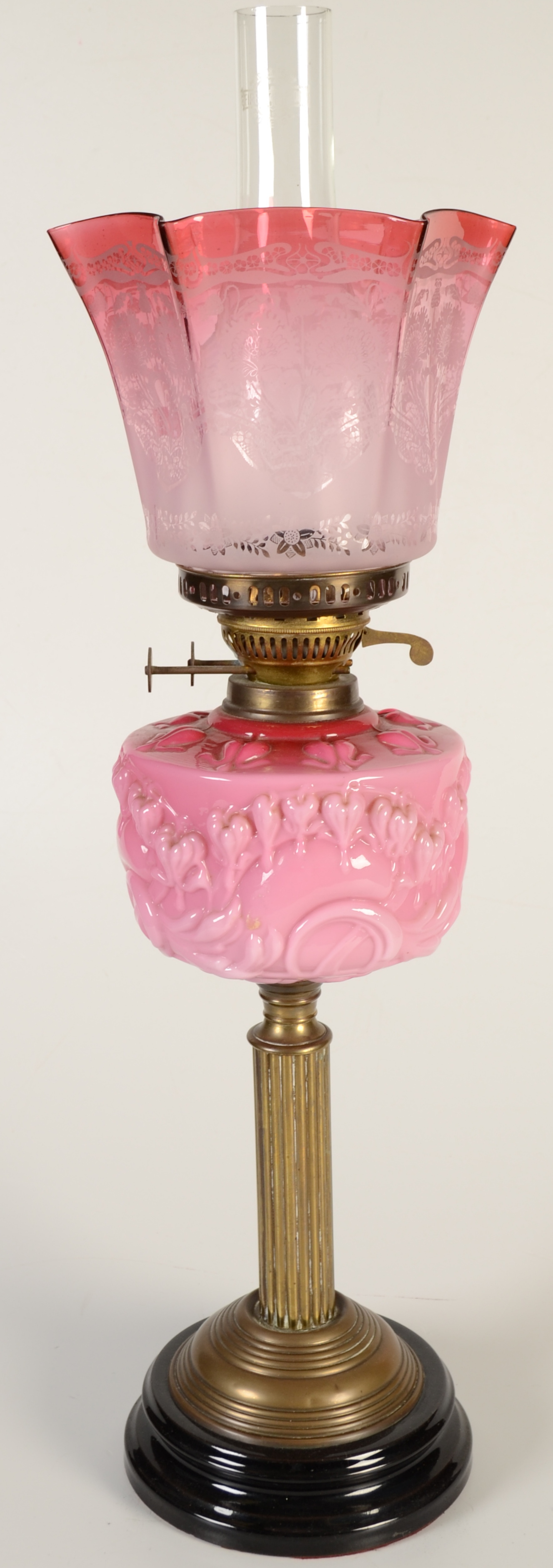 A Victorian oil lamp with a pink glass fount on a brass column and with an etched cranberry glass