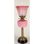 A Victorian oil lamp with a pink glass fount on a brass column and with an etched cranberry glass